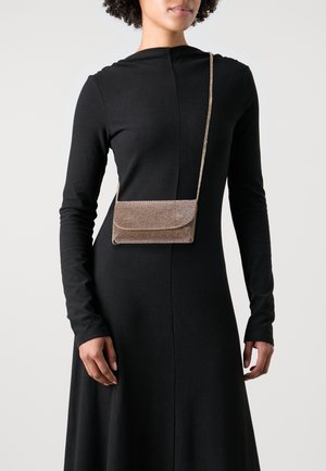 Złota torebka na ramię o teksturowanej powierzchni, prostokątnym kształcie i magnetycznym zamknięciu na klapę. Noszona do czarnej sukienki z długim rękawem.
