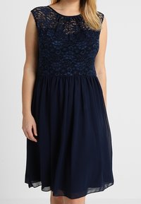 Robe bleu marine avec un corsage en dentelle, design sans manches, encolure ronde et jupe en chiffon fluide. Présente un revêtement texturé et une taille froncée.