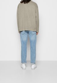 Överdimensionerad, ribbad ljusgrå tröja med rundad nederkant, kombinerad med rak benfade blå jeans och vita sneakers.