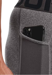 Grijze sportleggingen met een zijzak waarin een zwarte smartphone is geplaatst. De stof is glad met een textuurpaneel op de zak.