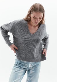 Maglione grigio a costine con scollatura a V e maniche lunghe, abbinato a pantaloni metallici azzurri. Tessuto morbido e vestibilità comoda.