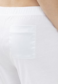 Witte broek met een gladde textuur, elastische tailleband en een kleine satijnen zak aan de achterkant, met een eenvoudig en strak ontwerp.