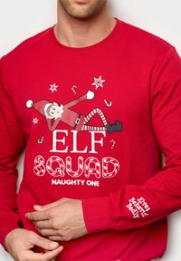 Rød langærmet skjorte med grafik af en ansigtet alv, teksten "ELF SQUAD" med slikstænger og snefnug, samt "Elves Behaving Badly" på ærmet.