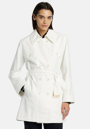 White cotton trench coat with double-breasted button closure, belted waist, large collar, and two front pockets. Smooth texture.