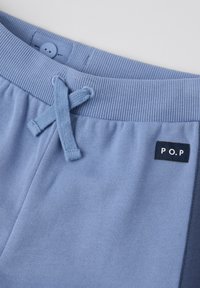 Lichtblauwe joggingsbroek met geribbelde tailleband, een aantrekkoordsluiting en een klein zwart etiket met de opdruk "P.O.P" aan de zijkant. Zacht katoenen materiaal.