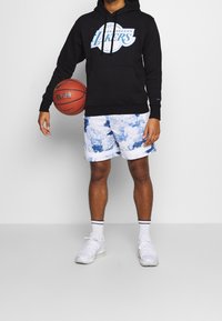 Czarna bluza z kapturem z logo "Los Angeles Lakers", w połączeniu z szortami w niebiesko-białe chmurki. Białe sneakersy z czarno-białymi skarpetkami w paski.