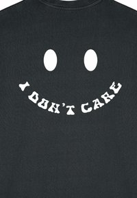Čierne tričko s veľkým bielym potlačeným usmievavým tvárou s dvoma oválnymi očami a textom "NEZÁLEŽÍ MI NA TOM" v hravom písmene.