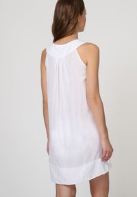 Vestido blanco sin mangas con una tela suave y ligera, que presenta un escote redondo, pliegues sutiles en la parte posterior y un dobladillo recto.