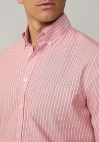 Camicia a righe rosse e bianche con colletto a bottoni, tasca sul lato sinistro del petto e logo ricamato in modo discreto sopra la tasca.