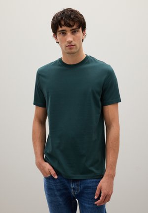 Camiseta de cuello redondo en verde oscuro, hecha de algodón suave. Manga corta y un ajuste relajado, combinada con unos jeans de mezclilla azul claro.