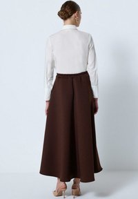 Brown, long, A-line skirt made from textured fabric with an elastic waistband, paired with a white button-up shirt.