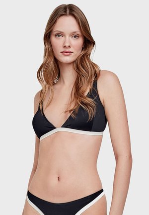 Bikini noir avec des accents blancs ; haut triangulaire et bas taille basse. Tissu lisse avec un design minimaliste et une bordure contrastante.