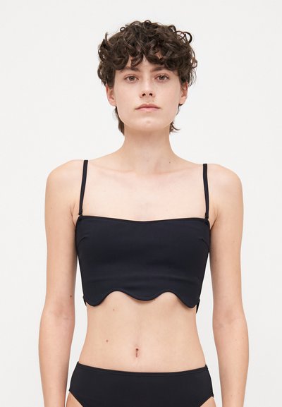 Top noir court avec bretelles fines, présentant un ourlet festonné et une texture lisse. Les détails incluent une silhouette ajustée et un design minimaliste.
