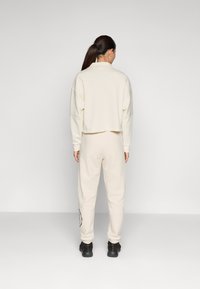 Cream-colored cropped sweatshirt with dropped shoulders paired with matching sweatpants. Features a side pocket and black logo accent.