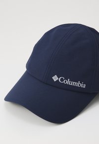 Cappellino da baseball blu navy realizzato in tessuto morbido, con una corona strutturata e un visiera appuntita; presenta un logo Columbia bianco sul lato.