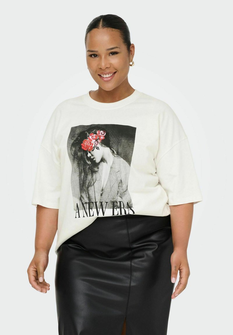 Camiseta de gran tamaño en color crema con un gráfico en blanco y negro de una mujer, acentos florales y el texto audaz "UNA NUEVA ERA", combinada con una falda de cuero negra.