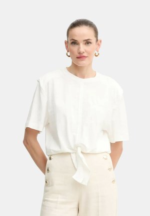 T-shirt bianco a maniche corte con dettaglio annodato sul davanti. Materiale in cotone morbido con vestibilità rilassata. Abbinato a pantaloni crema con dettagli a bottoni.