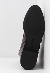 Bota de tobillo de ante gris con punta redondeada, cremallera lateral y suela de goma negra texturizada, con un sutil logo grabado en el costado.