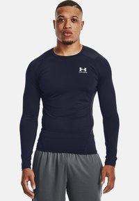 Mørkeblå langermet treningstrøye laget av glatt stoff, med en tettsittende design og en liten hvit Under Armour-logo på brystet.
