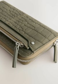 Grön texturerad plånbok med reptilmönster och släta accenter. Har en dragkedjestängning, dragflik och detaljer i silver.