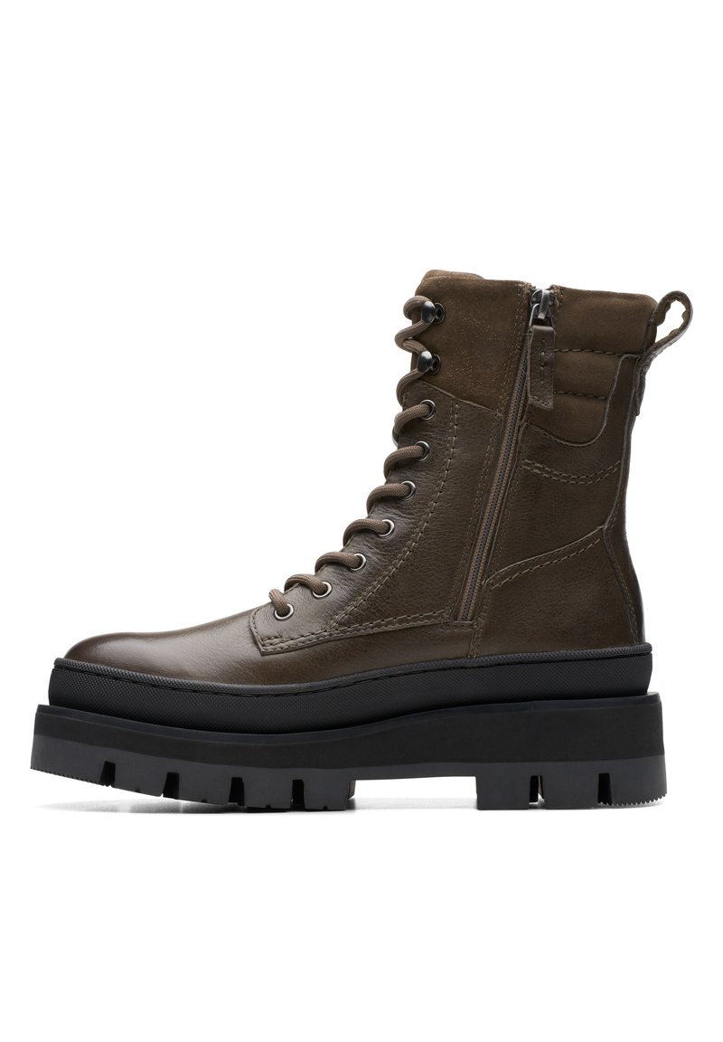 Botas de cuero marrón hasta el tobillo con cordones en la parte delantera, cierre lateral con cremallera y una suela negra gruesa con surcos profundos para mayor tracción.