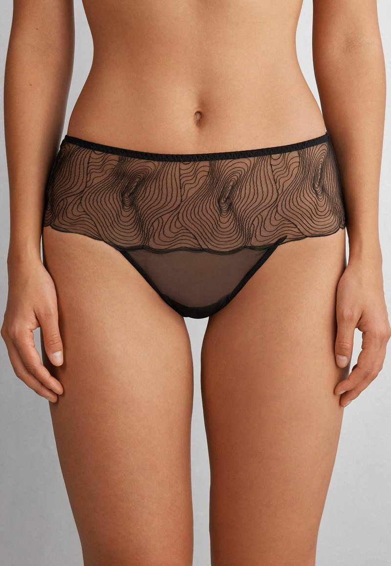 Zwarte doorschijnende lingerie met een golvend patroon, voorzien van een gestructureerd netpaneel aan de bovenkant en een bijpassend effen ondergedeelte.
