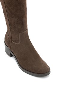 Brązowy zamszowy wysokich cholew but z ostrym noskiem i niskim, grubym obcasem. Posiada tonalne szwy i gładką, miękką teksturę.