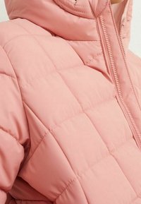 Giacca gonfiabile rosa trapuntata con colletto alto, chiusura con zip e tessuto testurizzato. Presenta cuciture a forma di rombo e superficie liscia.