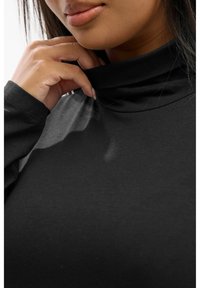 Czarny golf wykonany z gładkiego, elastycznego materiału z długimi rękawami. Zbliżenie podkreśla dekolt i fakturę.