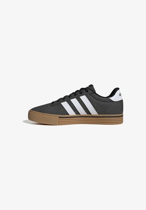 Baskets basses noires avec des bandes blanches Adidas et logo, semelle en caoutchouc naturel et lacets noirs sur fond blanc.