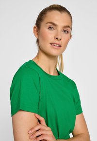 Grøn bomulds T-shirt med korte ærmer, rund halsudskæring og glat overflade; bæres afslappet, med fokus på halsudskæringen og skulderen.