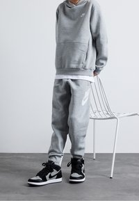 Ljusgrå huvtröja med en framficka, matchande med joggingbyxor som har en vit Nike-logotyp. Svart och grå högskor.