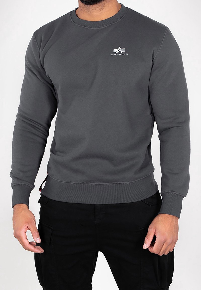 Sudadera gris hecha de tela suave, con cuello redondo, puños y dobladillo acanalados, y un pequeño logo blanco en el pecho.