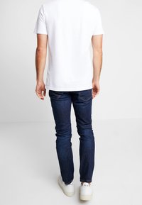 Camiseta blanca de manga corta combinada con jeans azul oscuro y zapatillas blancas. La camiseta tiene un diseño sencillo, con un cuello redondo y un corte recto.