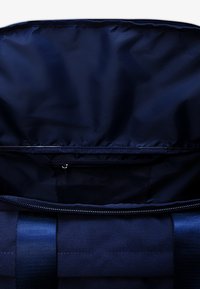 Bolsa de tela azul marino con un forro interior liso y brillante. Cuenta con un compartimento con cremallera y correas de tela resistentes. El interior tiene un bolsillo de malla.