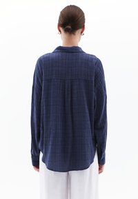 Mörkblå, oversized rutig skjorta med mjuk textur, långa ärmar och krage. Bakdelen har en yoke-söm och avslappnad passform.