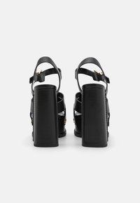 Sandale negre cu toc înalt, cu un toc masiv, având curele late și o cataramă aurie pe curea. Textură din piele netedă.