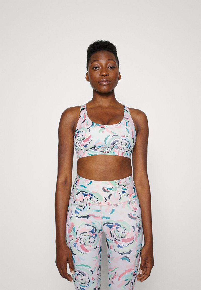 Conjunto de roupa desportiva com padrão floral em cores pastel. O sutiã desportivo possui uma banda larga e decote arredondado, complementado por leggings de cintura alta.