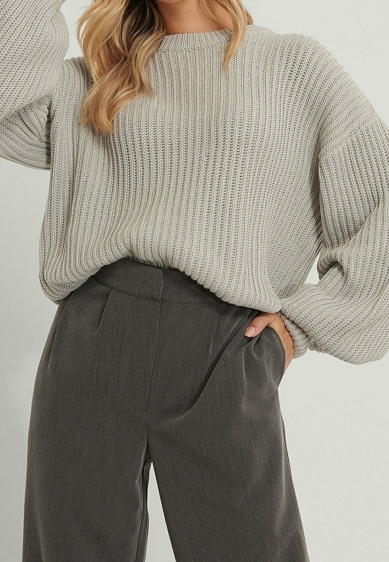 Maglione grigio chiaro lavorato a maglia con una texture a coste, maniche larghe e scollo tondo, abbinato a pantaloni su misura grigio scuro.