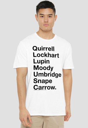 Young man wearing a white T-shirt with black text listing names: Quirrell, Lockhart, Lupin, Moody, Umbridge, Snape, Carrow.