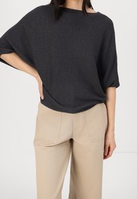 Ciemnoszary, teksturowany sweter z szerokim dekoltem i luźnym krojem, zestawiony z jasnobeżowymi spodniami o prostych nogawkach z bocznymi kieszeniami.