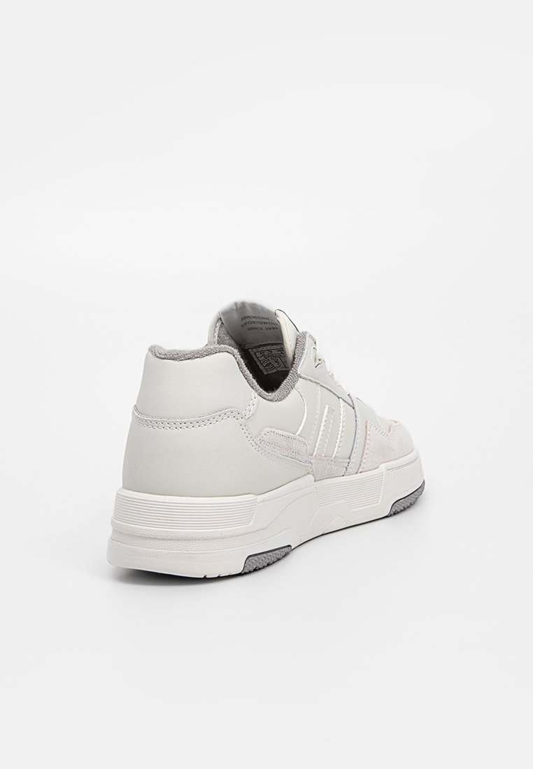 Weißer und grauer Sneaker, der die Rückseite und die Seite zeigt, mit strukturierten Paneelen, Schnürsenkeln und einer gemusterten Gummisohle.