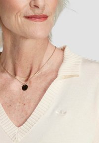 Pull créme à col en V avec des bords ribbed et un petit logo en relief. Un collier élégant et délicat avec un pendentif circulaire.