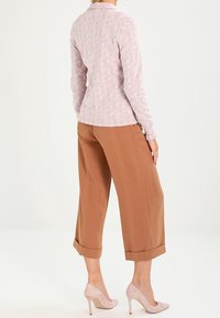 Ljusrosa mönstrad långärmad topp i kombination med beige vida byxor, uppvikta ärmar och nude högklackade skor.