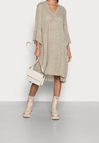 Robe beige à motifs floraux avec un col en V et des manches en cloche, associée à des bottines crème et un sac à main texturé crème.