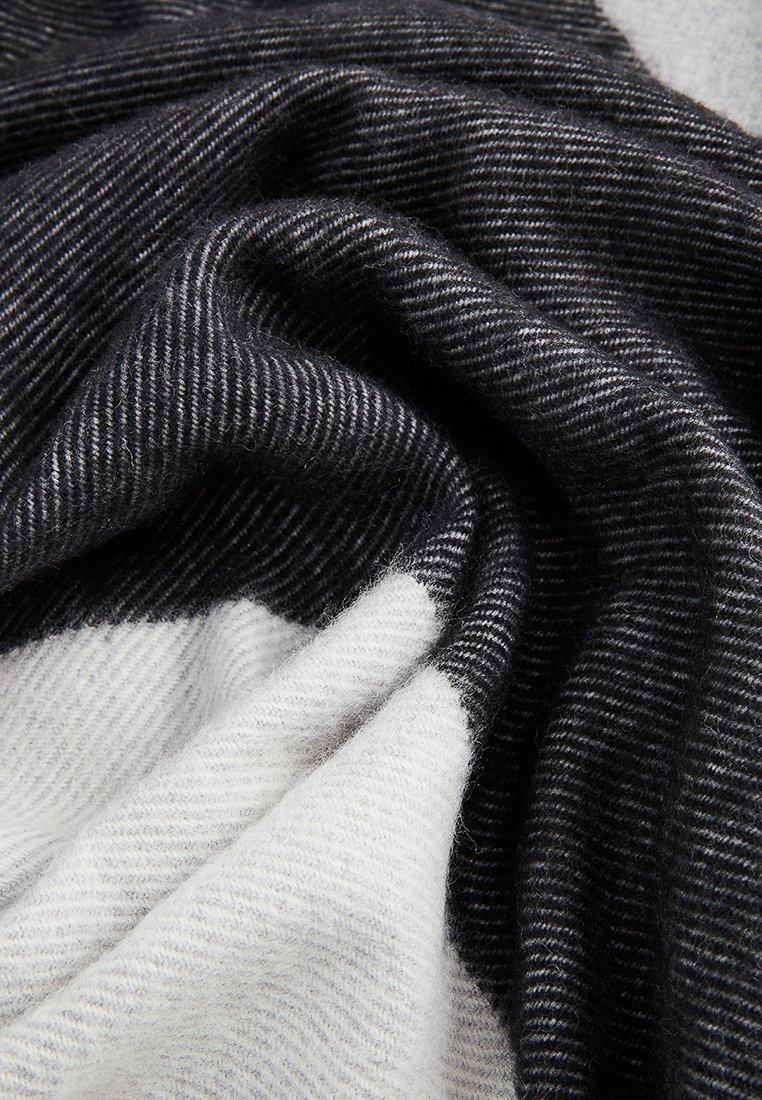 Weiches Wollgewebe mit schwarz-weißen Streifenmustern, in sanften Falten präsentiert, die Textur und Kontrast hervorheben.