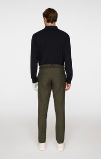 Męska czarna koszulka polo z długim rękawem połączona z oliwkowymi spodniami. Spodnie mają teksturowany pasek i tylne kieszenie. Białe sneakersy dopełniają stylizację.