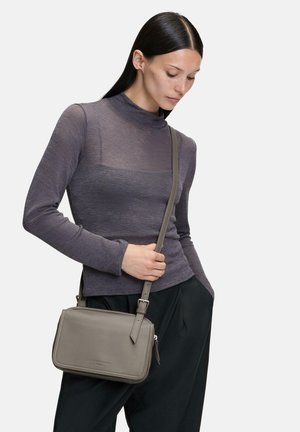 Graue Leder-Crossbody-Tasche mit rechteckiger Form, Reißverschluss und verstellbarem Riemen, kombiniert mit einem enganliegenden lila Longsleeve.