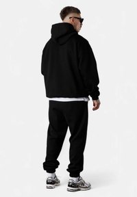 Sweatshirt à capuche noir et joggers assortis, dotés de poignets côtelés et d'une coupe décontractée. Porté avec un t-shirt blanc et des baskets à accents argentés.