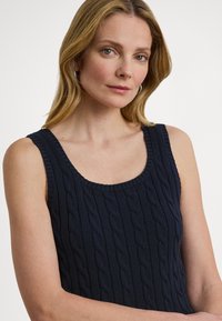 Mörkblå stickad linne med kabelstickningsmönster, breda band och en rundad urringning. Slät textur med ribbade kanter.